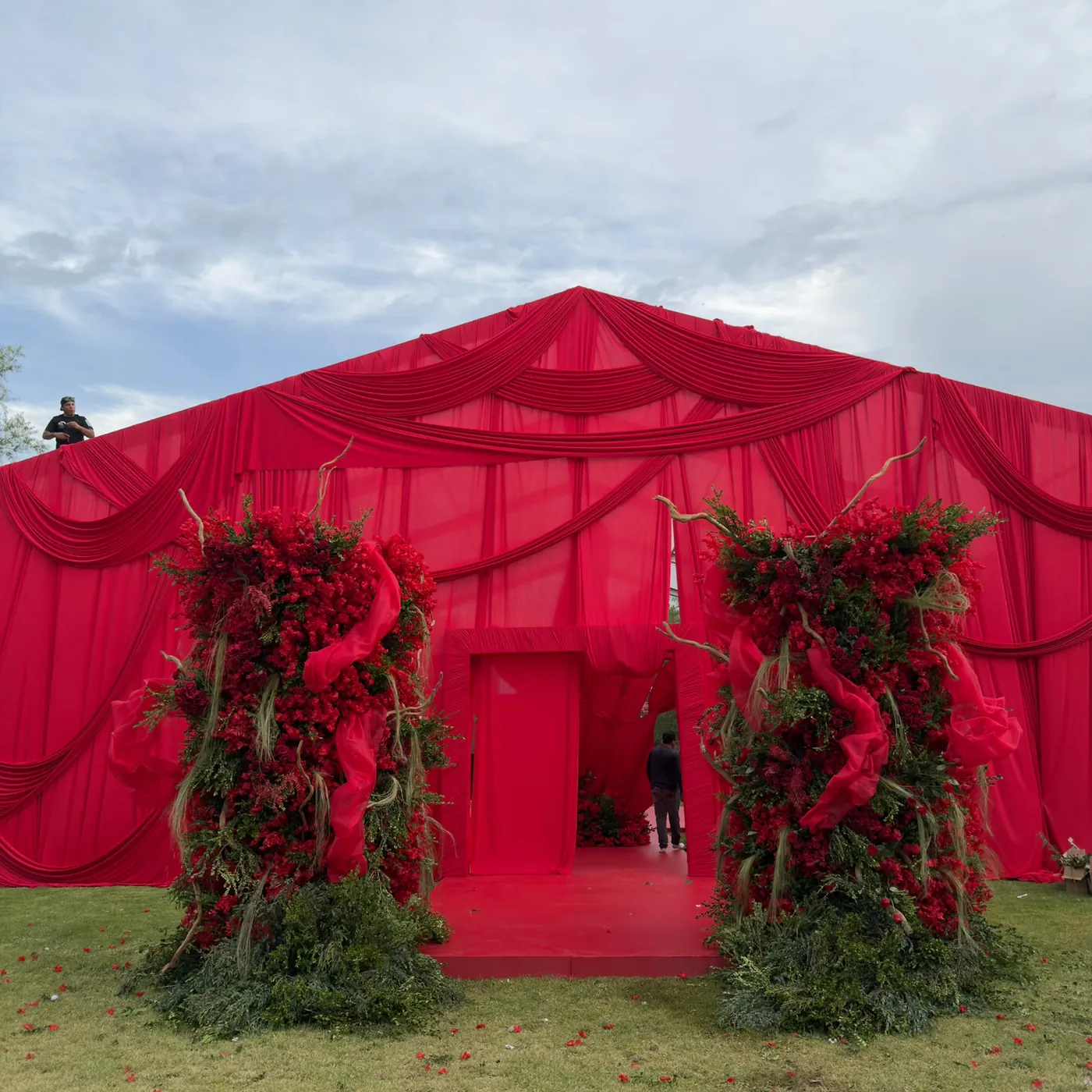 Carpa decorada con tela roja y arreglos florales monumentales en la entrada